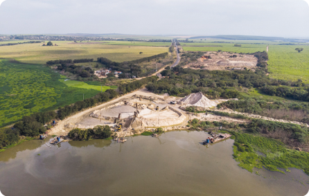 Fotografia. Vista aérea de um rio com areia e terra gramada na margem. Ao fundo, contém mais areia e vegetações de cores diferentes.