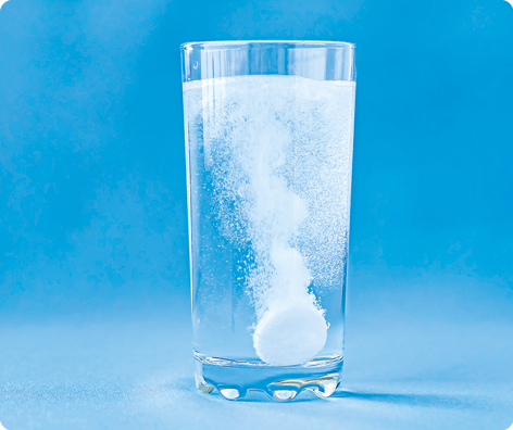 Fotografia. Um copo transparente com água e comprimido efervescente.