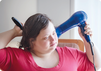 Fotografia. Uma menina, representada do peito para cima, segurando sobre o cabelo uma escova e um secador.