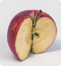 Fotografia. Uma maçã vermelha cortada ao meio com sementes à mostra e interior escurecido.