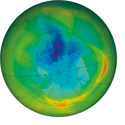 Ilustração. Representação do globo terrestre com o Polo Sul ao centro e a camada de ozônio sobre essa região. Sua cor é predominantemente verde nas bordas, com trechos amarelos, laranja e vermelhos, e uma região azul no centro.