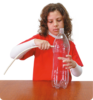 Fotografia de uma criança, vista da cintura para cima, segurando uma garrafa de plástico sem tampa em uma das mãos e com a outra colocando uma mangueira na lateral da garrafa.