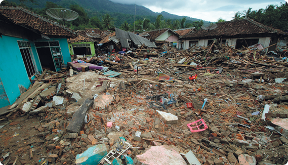 Fotografia de um vilarejo com escombros de construções e casas em volta, com algumas delas danificadas.