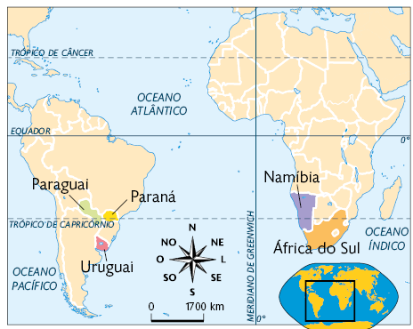 Mapa-múndi mostrando a América do Sul e a África, com indicações de alguns locais que estão aproximadamente na altura do trópico de capricórnio. Na América do Sul estão indicados dois países, o Paraguai e o Uruguai, e também o estado do Paraná. Na África estão indicados dois países, a Namíbia e a África do Sul. Na parte de baixo do mapa está a rosa dos ventos, a escala com a indicação zero e 1700 quilômetros, e no canto inferior direito uma miniatura do mapa-múndi, com destaque para a região apresentada.