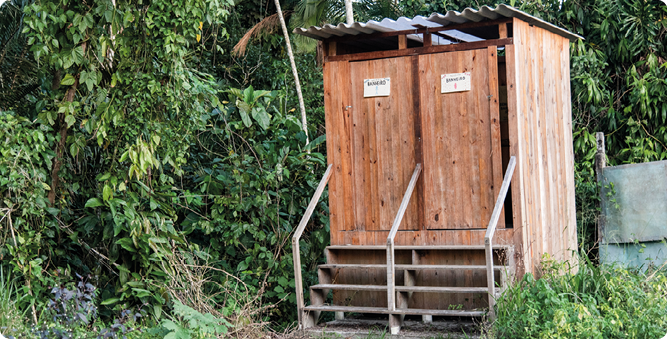 Fotografia de duas construções de madeira, uma ao lado da outra, compostas por três paredes, telhado e uma porta com placas, à frente uma escada de acesso. E no entorno vegetação.