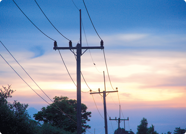 Fotografia de postes com cabos elétricos passando por eles. Os postes estão alinhados e os cabos formam uma curva para baixo entre eles.