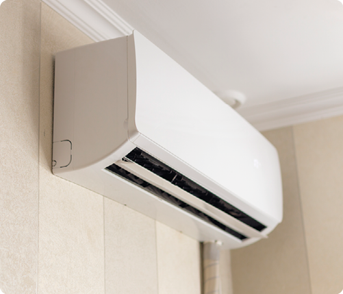 Fotografia de parte de um equipamento de ar condicionado que fica do lado interno do ambiente, preso à parede, próximo ao teto, com formato retangular e saída de ar na parte inferior.