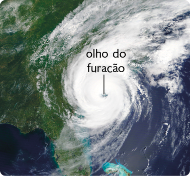 Fotografia. Vista do planeta Terra do espaço. Uma porção da imagem apresenta coloração verde e outras azul. Também há uma região com coloração branca, em formato de espiral, sobrepondo partes das regiões verde e azul. No centro da espiral esbranquiçada está o olho do furacão, que é uma região circular sem coloração branca.