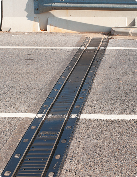 Fotografia de um trecho de uma rua pavimentada, que se estende horizontalmente. No meio, há uma faixa de estrutura metálica que une as partes pavimentadas.