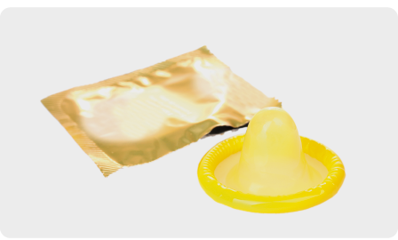 Fotografia. Preservativo masculino, formado por um material de coloração transparente. Ele tem formato cilíndrico e está enrolado. Ao lado, encontra-se a embalagem.