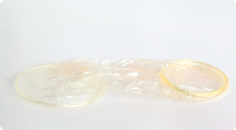 Fotografia. Preservativo feminino, formado por um material transparente, é comprido e possui argolas em ambas as extremidades.