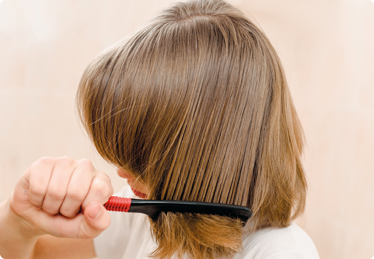 Fotografia. Uma pessoa penteando os cabelos com um pente de plástico.
