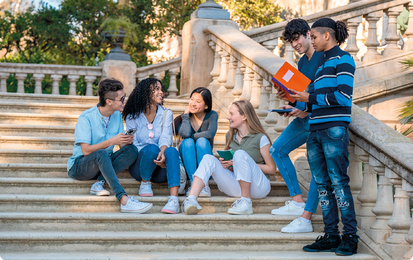 Fotografia de um grupo de jovens conversando. Há três moças e um rapaz sentados nos degraus de uma escadaria, e, próximo ao corrimão, há dois rapazes em pé.