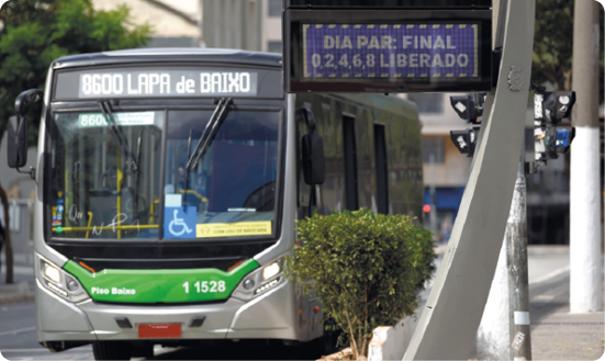 Fotografia de um ônibus em uma rua, e à frente, uma placa com o seguinte texto escrito: 'Dia par: final 0, 2, 4, 6, 8 liberado'.