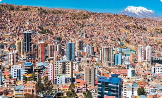 Fotografia. Vista de um local com muitos prédios e casas. Ao fundo, há uma montanha com gelo no topo.