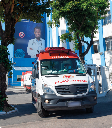 Fotografia. Uma ambulância, veículo alongado, de cor branca, com teto elevado na cor vermelha. Possui luzes vermelhas nas laterais. Na parte superior, encontra-se escrito 'SAMU 192' de forma invertida horizontalmente, com os caracteres na seguinte ordem, da esquerda para direita: 2 9 1 U M A S, enquanto no capô está escrito 'AMBULÂNCIA' de forma invertida horizontalmente, com os caracteres na seguinte ordem, da esquerda para direita: A I C N Â L U B M A.