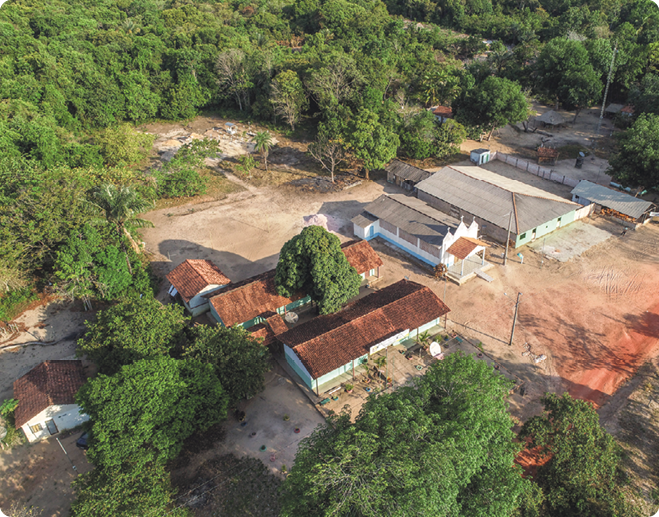 Fotografia aérea de uma comunidade, ao centro construções e no entorno vegetação.