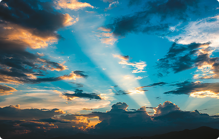 Fotografia do céu ao entardecer, com algumas nuvens e o Sol encoberto por elas. A partir de alguns espaços entre as nuvens há trechos do céu iluminados pelo Sol, exibindo coloração esbranquiçada.