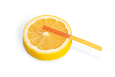 Fotografia de uma fatia de limão e uma fita de papel amarela com uma extremidade em contato com o limão. Nessa extremidade a fita de papel apresenta uma coloração avermelhada.