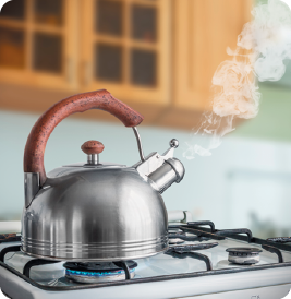 Fotografia de uma chaleira sobre a chama de uma boca fogão, e uma névoa branca saindo do bico lateral.