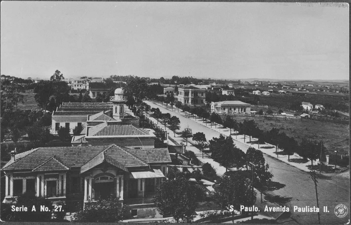 Fotografia em preto e branco. Extensa avenida com muitas árvores nas margens e casarões nas duas laterais.