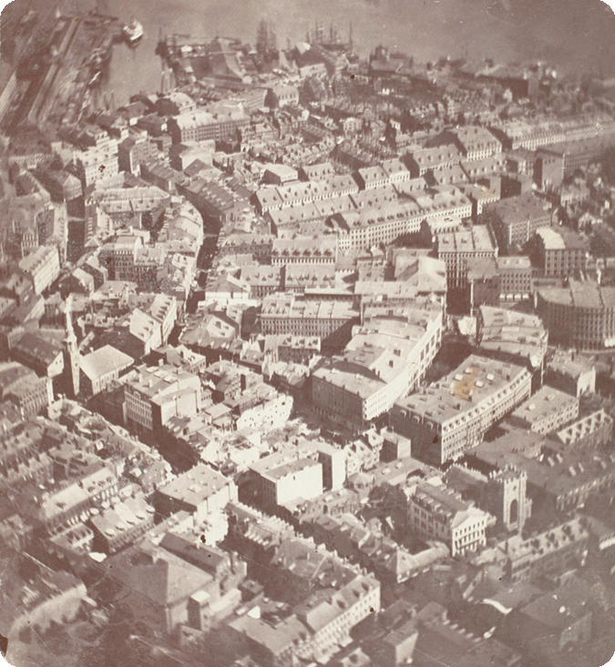 Fotografia em preto e branco. Uma cidade com muitas construções dispostas em quarteirões.