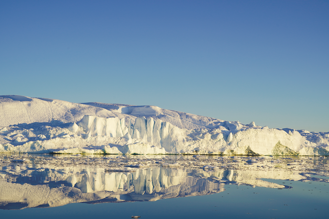 Fotografia. Uma grande geleira cercada pelo mar que reflete sua paisagem.