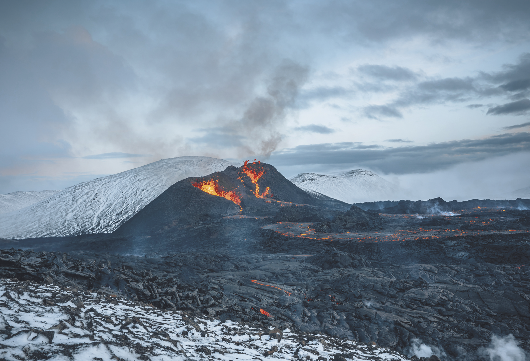 Fotografia. Um vulcão expelindo lava e fumaça. Ao redor dele há neve.