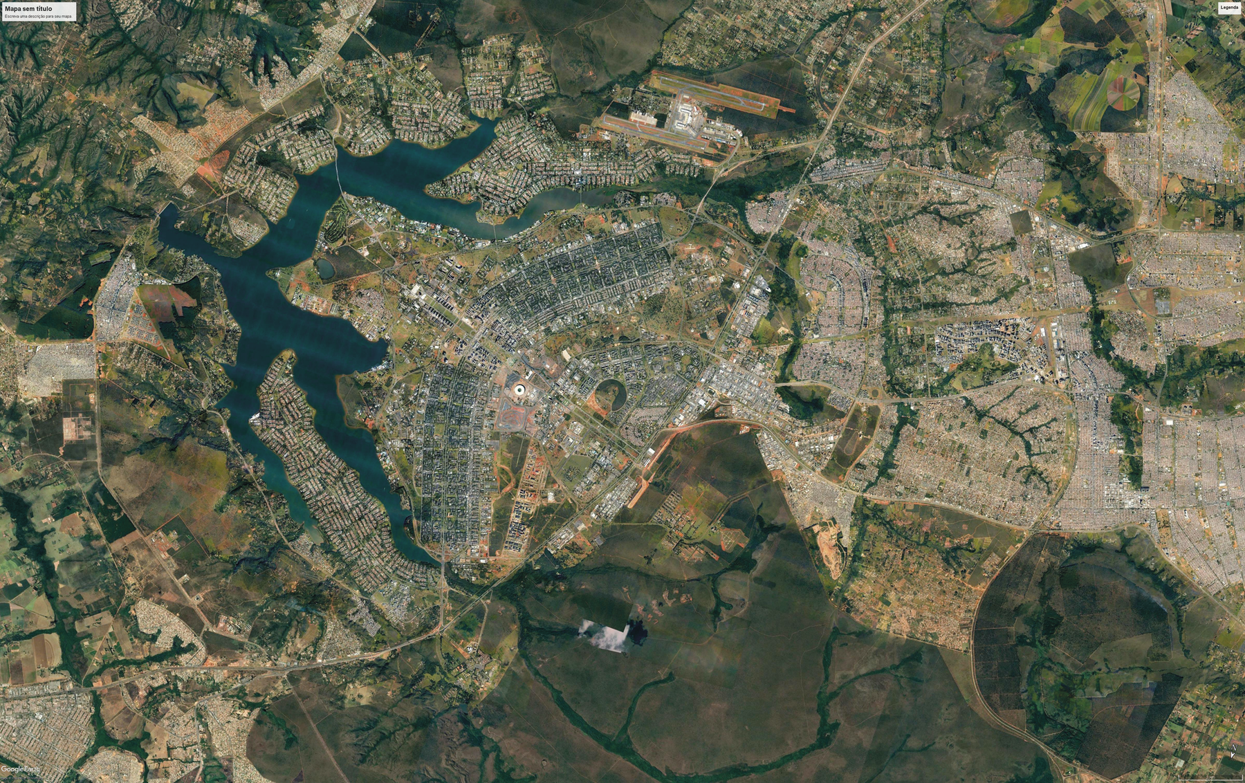 Fotografia. Vista aérea. Uma cidade com construções com um formato semelhante a asas. Ao redor há outras construções, áreas cobertas por vegetação e rios.