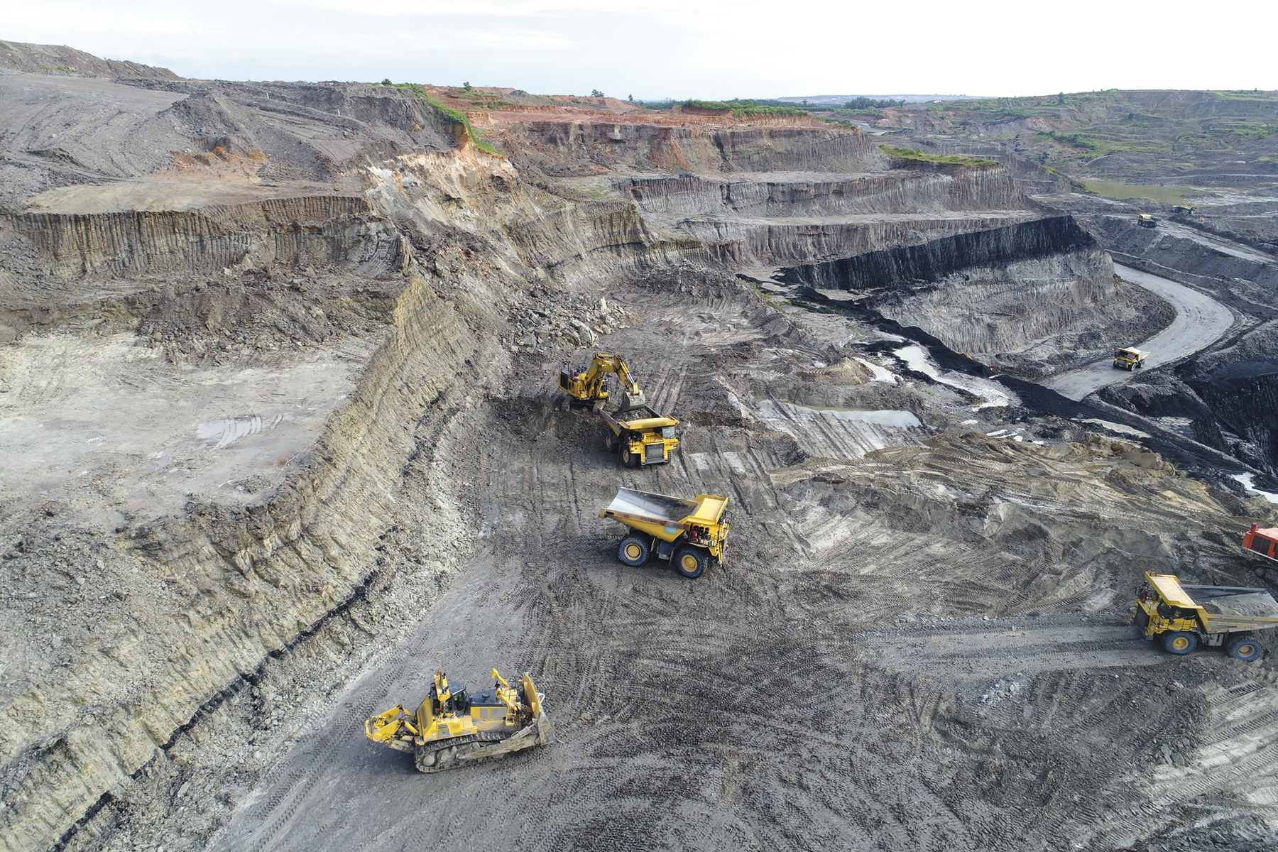 Fotografia. Tratores em meio a uma mina de carvão. Há desníveis no solo cinzento.