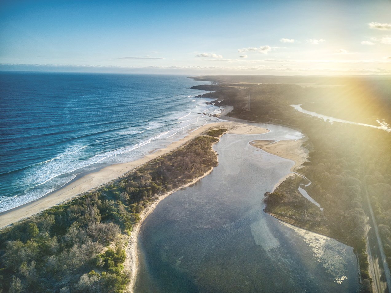 Fotografia. Vista de cima. O curso de um rio sinuoso desaguando no mar. Há áreas cobertas com vegetação entre eles.