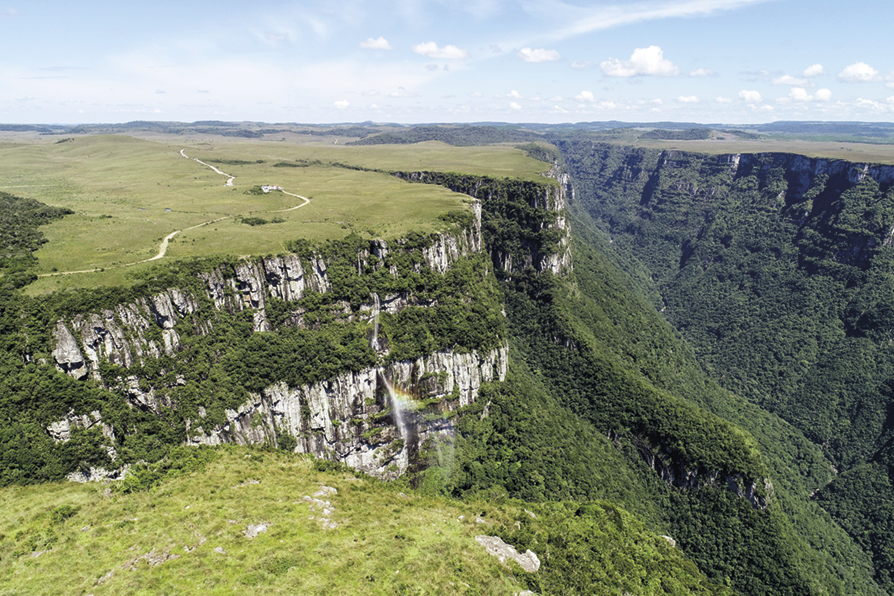 Fotografia A. Formação rochosa com o topo plano coberto por vegetação rasteira. Em frente a ele há um vale profundo coberto por vegetação densa.