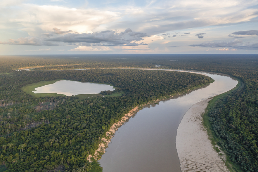 Fotografia B. Vista de cima. O curso de um rio sinuoso com as margens repletas de vegetação. À esquerda, entre a floresta há um lago.