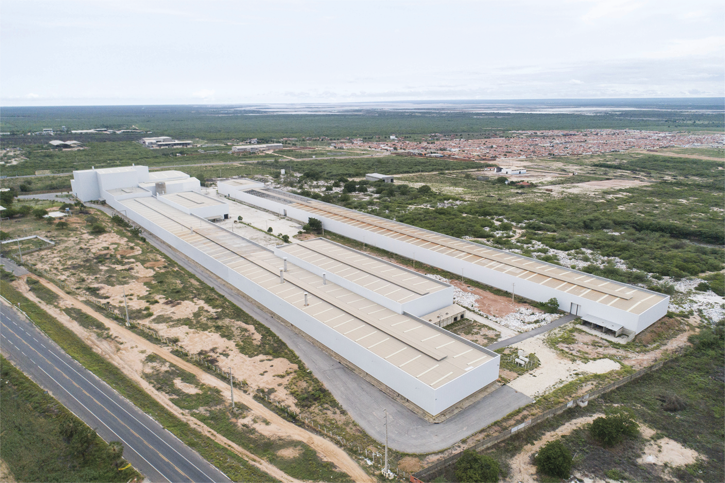 Fotografia A. Galpões extensos e paralelos. Ao redor, uma cidade e áreas cobertas por vegetação.