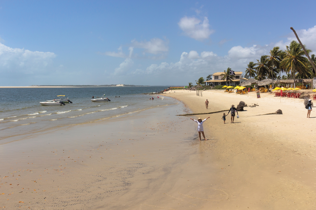 Fotografia B. Uma praia com algumas pessoas na faixa de areia e barcos no mar.