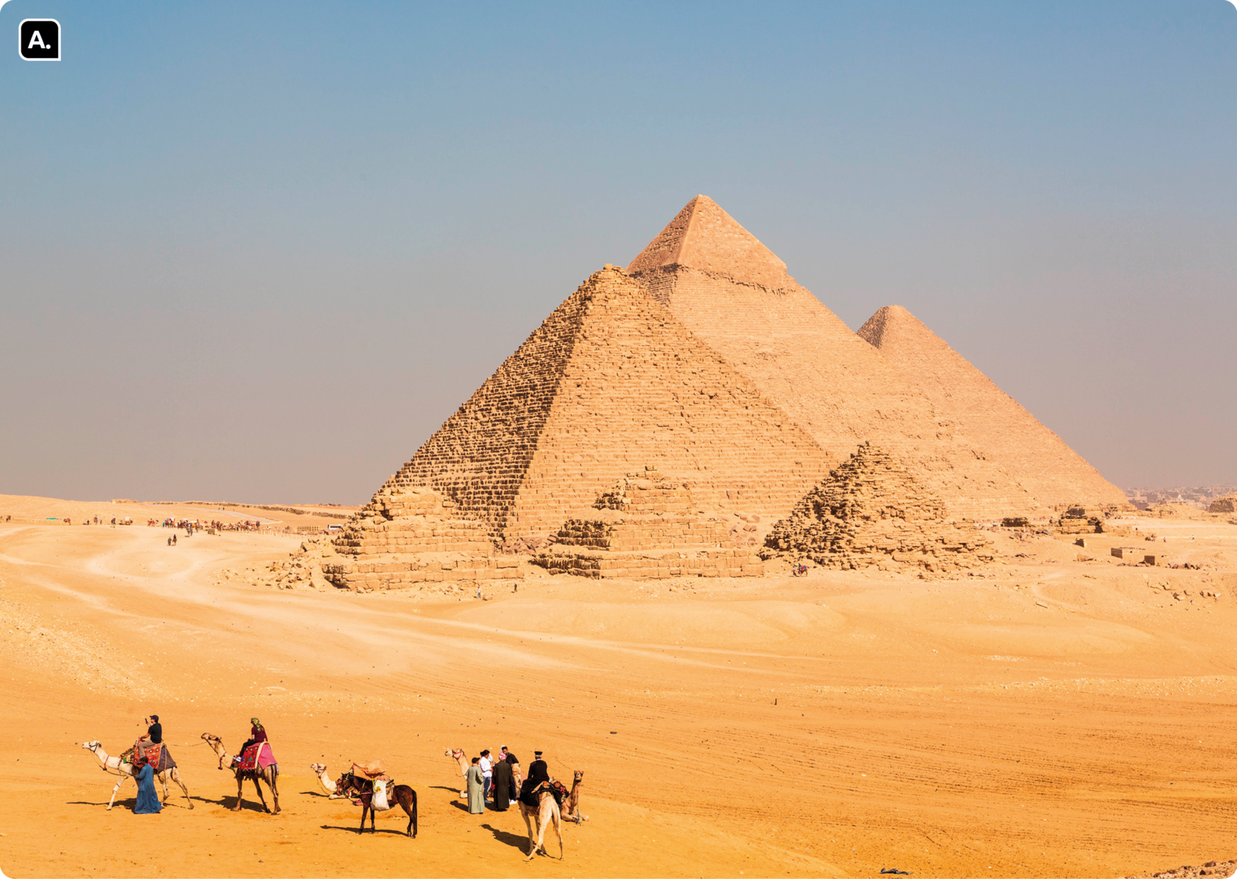 Fotografia A. Pessoas caminhando por um deserto em camelos. Há um cavalo entre elas. Ao fundo, há três grandes pirâmides e três menores em frente.