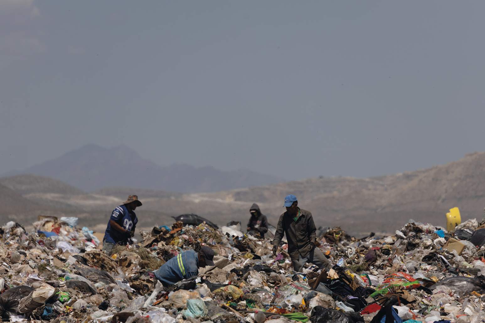 Fotografia. Pessoas em meio a uma área coberta por lixo.