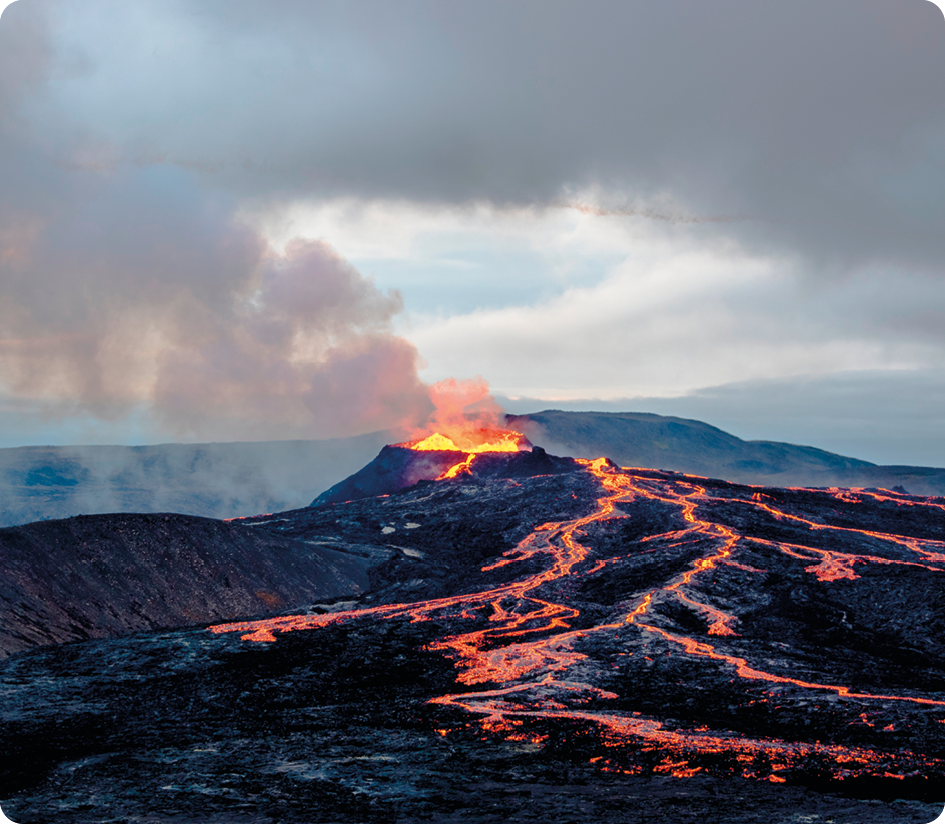 Fotografia. Um vulcão expelindo lava. Há magma escorrendo por sua encosta e muita fumaça saindo dele.