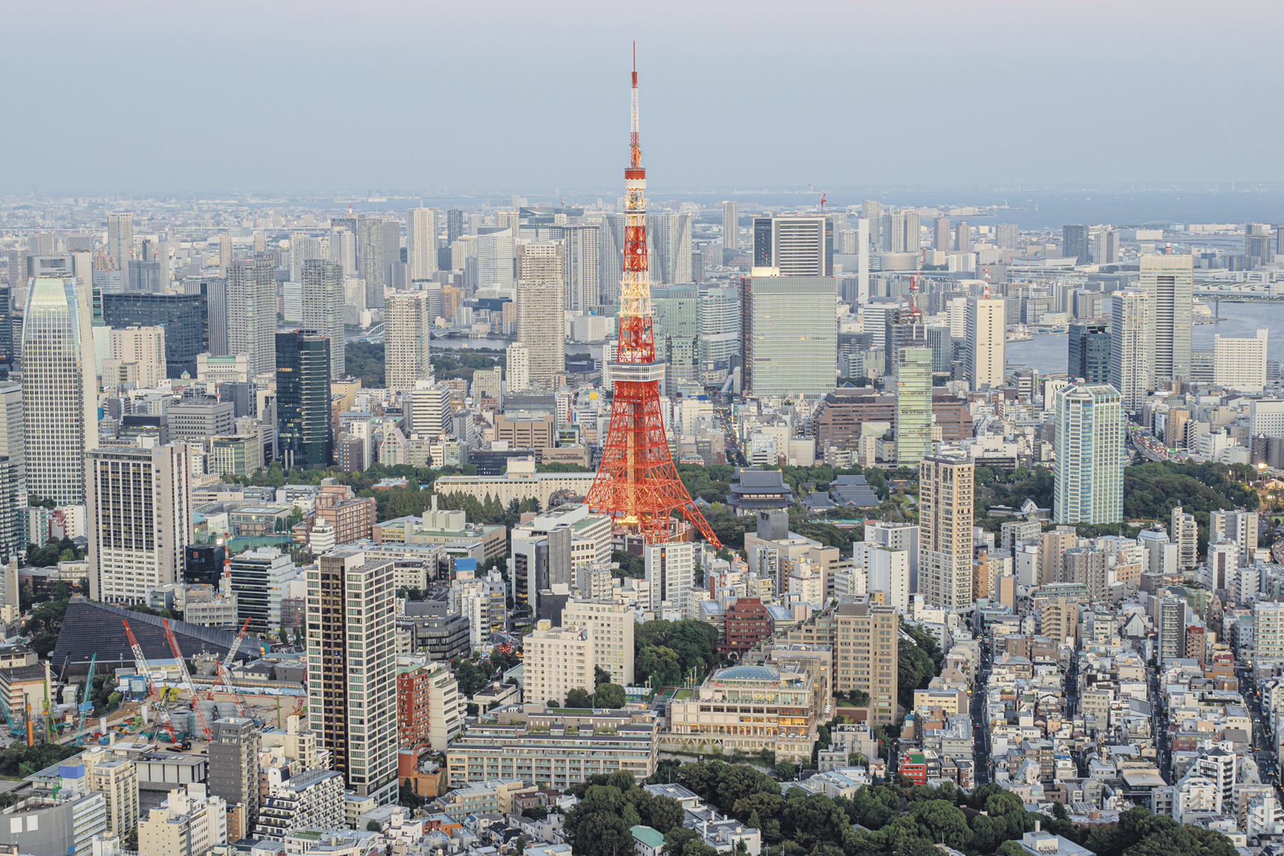 Fotografia. Vista do alto. Uma cidade repleta de edifícios com uma antena grande e laranja ao centro.