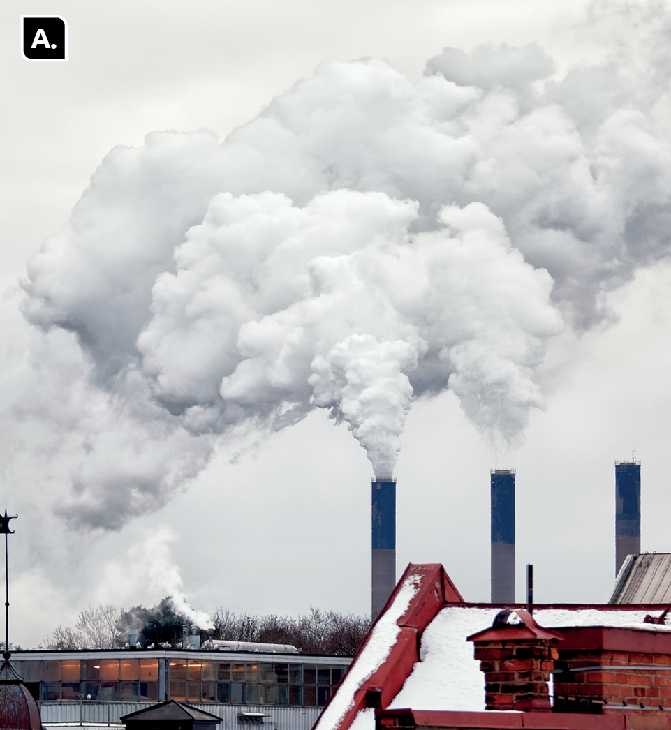 Fotografia A. Destaque para chaminés compridas expelindo uma grande quantidade de fumaça no céu. Há construções ao redor.