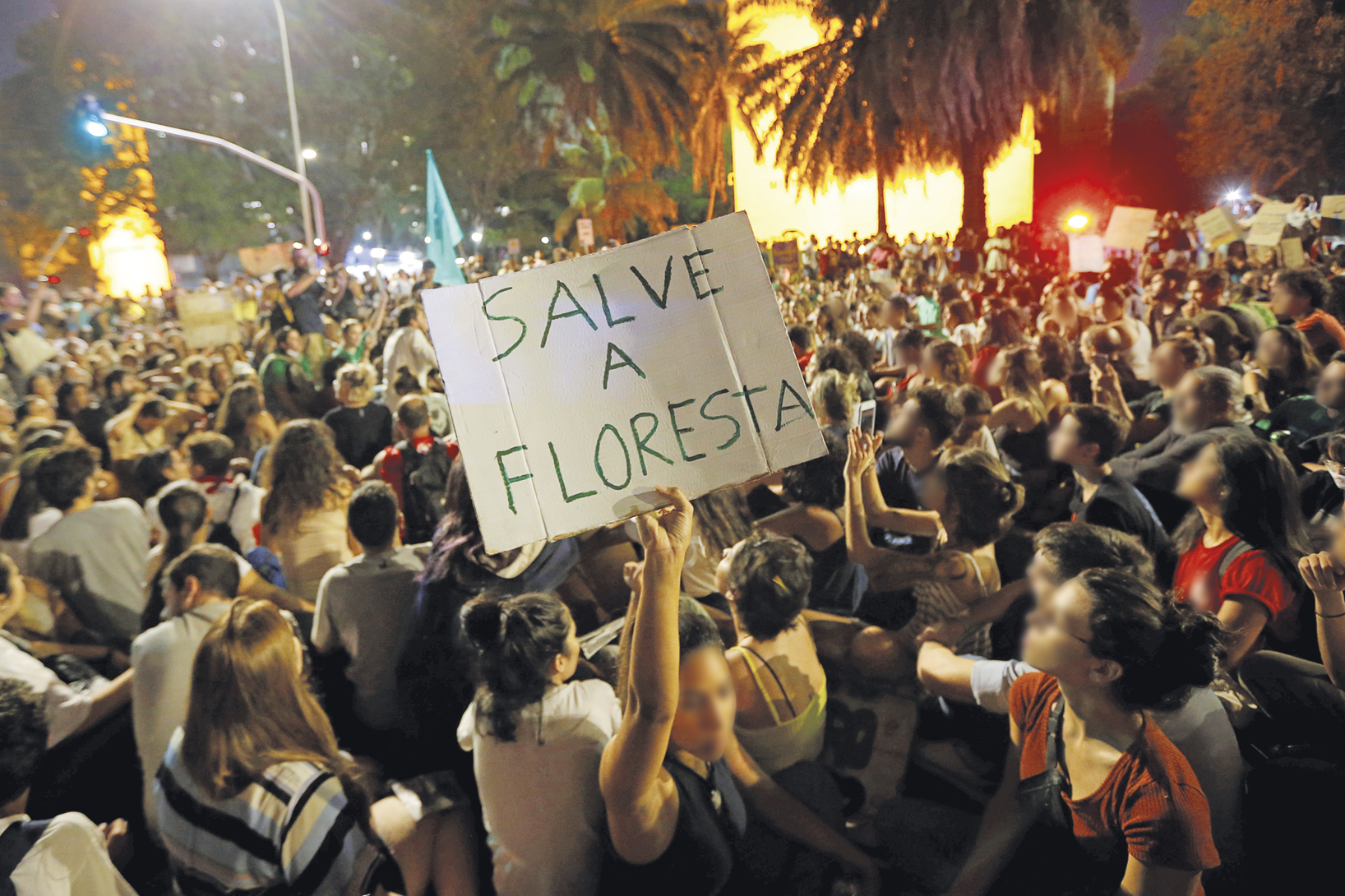 Fotografia. Uma manifestação com muitas pessoas, uma delas segura um cartaz com a frase: SALVE A FLORESTA.