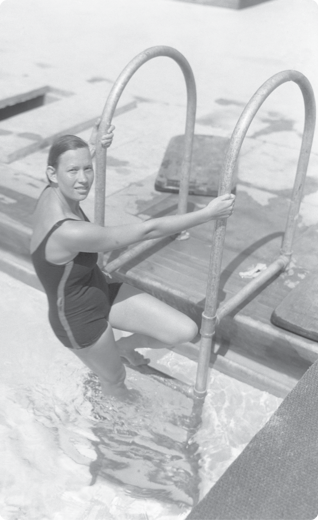 Fotografia em preto e branco. Maria Lenk, mulher com cabelos presos, usando maiô. Ela está segurando uma escada na beira da piscina.