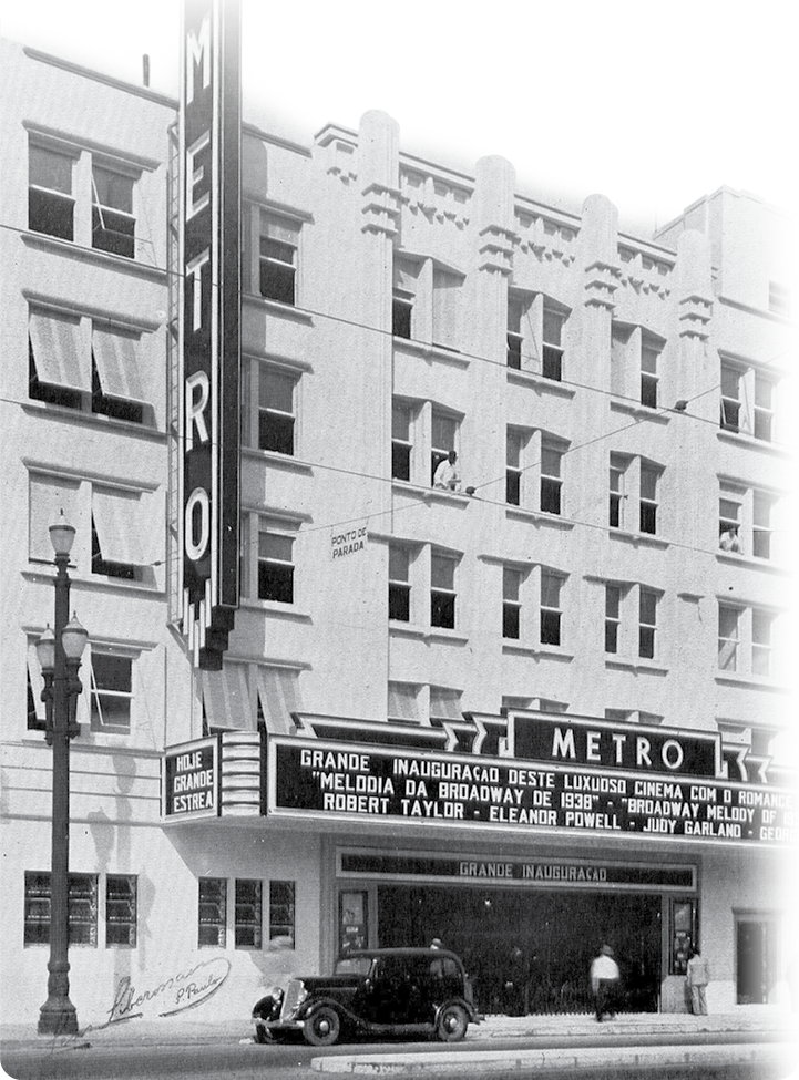 Fotografia em preto e branco. Fachada de um prédio com placas na diagonal e na parte central, com o texto: METRO.