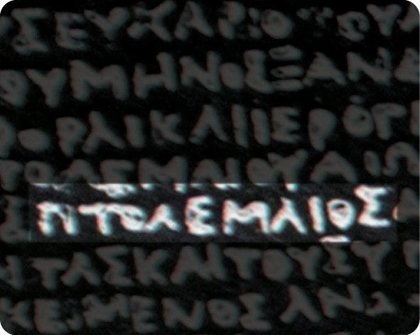 Fotografia. Destaque de recorte da Pedra de Roseta com elementos de escrita em grego.