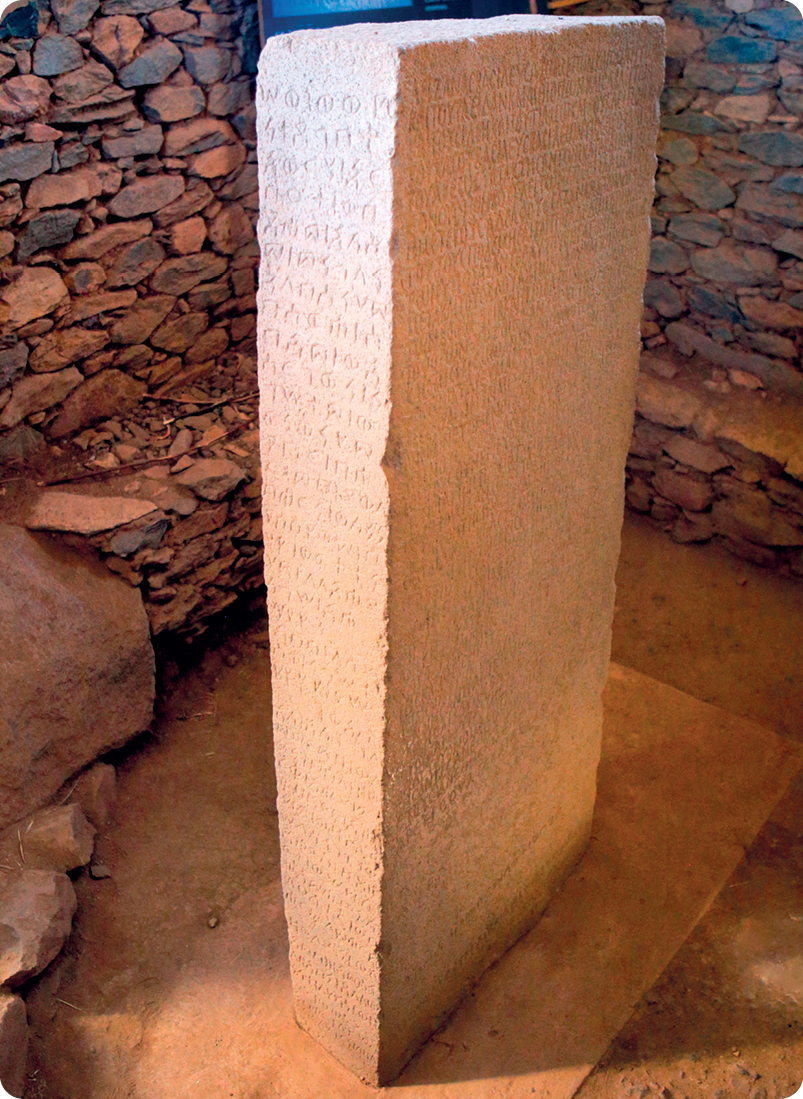 Escultura. Uma pedra em formato retangular com diversas inscrições.