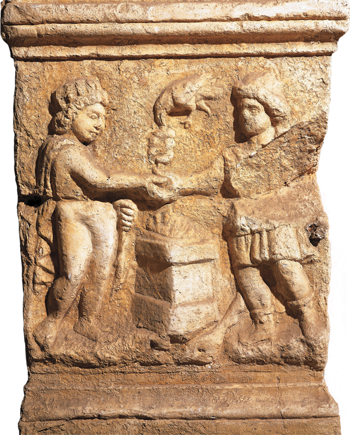 Fotografia. Detalhe em relevo de um altar. Duas pessoas, uma de frente para a outra, com a mãos sobre um altar.