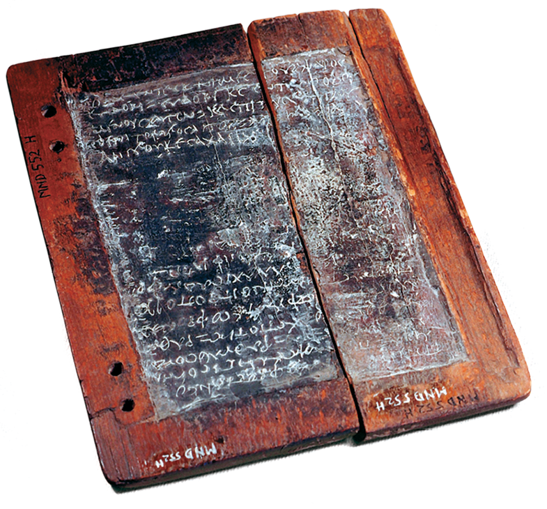 Fotografia. Tabuleta em forma retangular de madeira e bronze com elementos da escrita latina em branco. Há uma rachadura no meio da tabuleta.