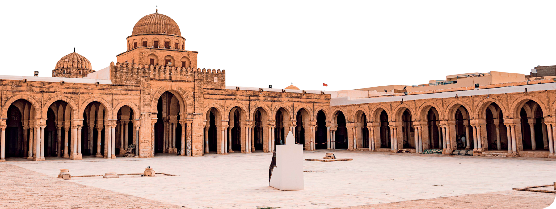 Fotografia. Fachada de mesquita, composta por paredes com diversas colunas e arcos. Há duas cúpulas pequenas no teto. Na frente, um pátio com um bloco branco no centro.