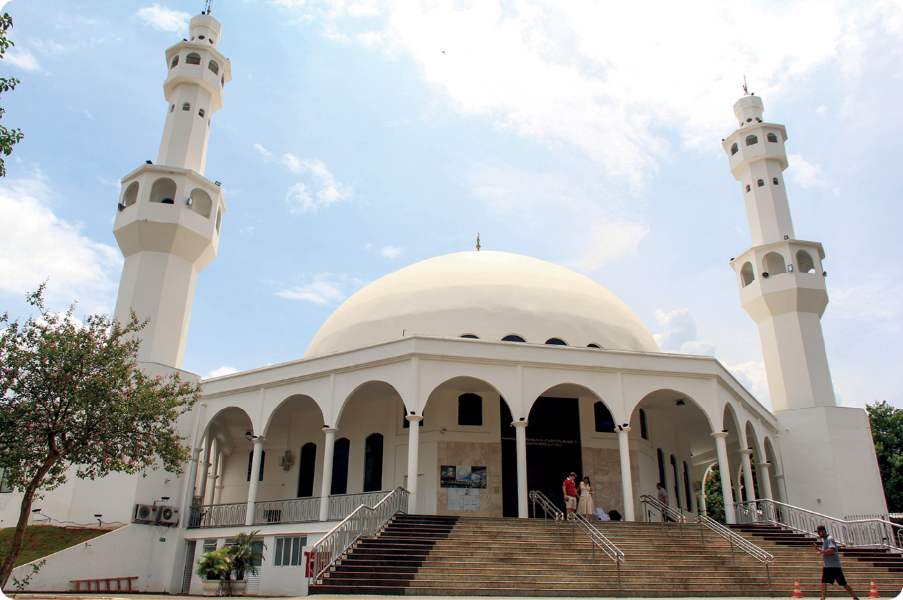 Fotografia. Mesquita Omar, construção branca, com uma cúpula central e duas torres. A fachada é comporta por várias colunas e arcos. Na frente, uma escadaria.