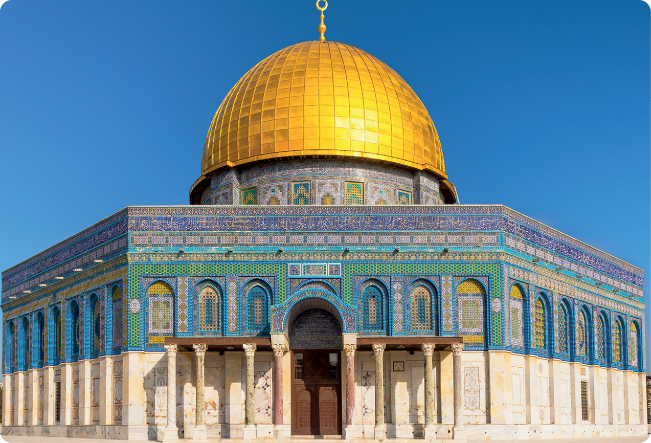 Fotografia. Fachada de mesquita com cúpula dourada. Na parte exterior, colunas ornamentadas e detalhes em azul, verde e amarelo. Ao centro, uma porta de madeira.